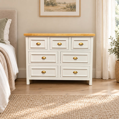 Cómoda Aval Deluxe de MGR Muebles con 7 cajones, madera de pino blanca y cubierta natural en un dormitorio rústico.